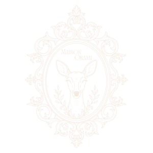 Logo Maison Okami couleur champagne avec tête de biche dans un cadre ornemental baroque.